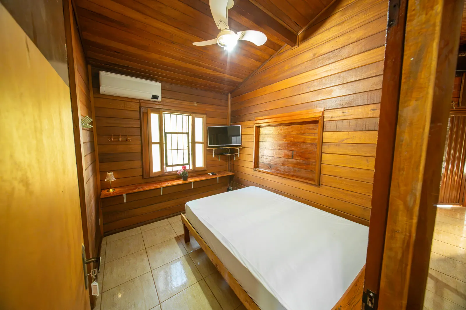 Suíte em madeira com cama de casal, TV e ar-condicionado